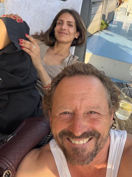 A couple enjoys a sunny day on a rooftop terrace in Oudeschans, Uilenburg, Amsterdam, with the man taking a cheerful selfie